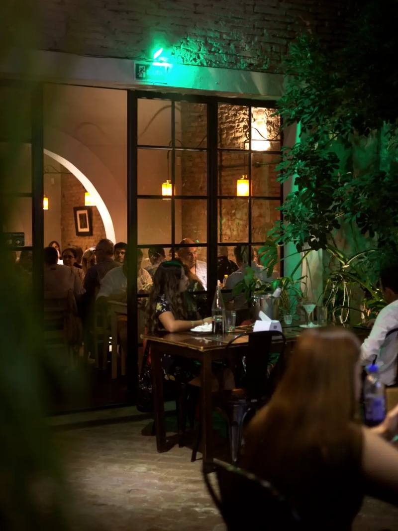 La entrada de Viejo Mercado de noche, con plantas, puertas de vidrio y el salón lleno de fondo