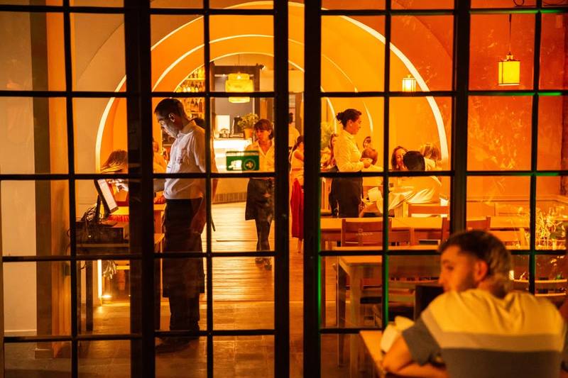 El salón de Viejo Mercado visto desde la ventana: arcos blancos, mesas de madera y luz cálida de lámparas
